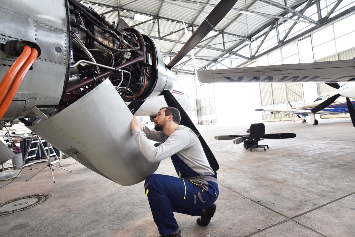 Technicien aéronautique inspectant et travaillant sur les composants internes d'un moteur d'avion dans une installation de maintenance. 